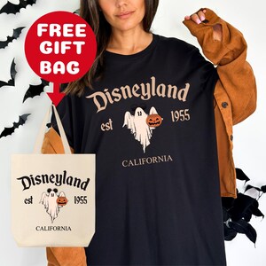 May include: Black t-shirt with a white graphic of a ghost holding a jack-o-lantern. The graphic says "Disneyland est 1955 California". A white tote bag with the same graphic is included.