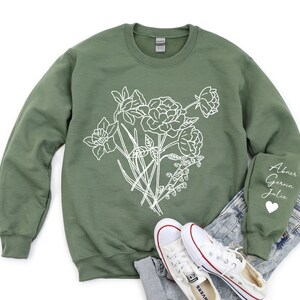 May include: A green sweatshirt with a white floral design and the names "Abner, Gerwin, Julie" on the sleeve.