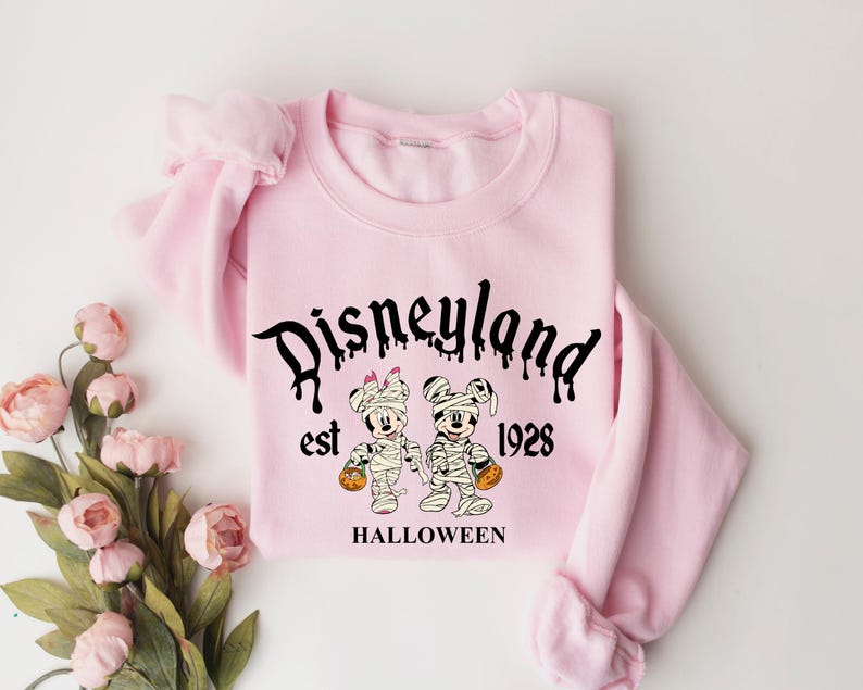 May include: Pink sweatshirt with a black graphic of Mickey Mouse and Minnie Mouse dressed as mummies. The graphic says "Disneyland est 1928 HALLOWEEN".