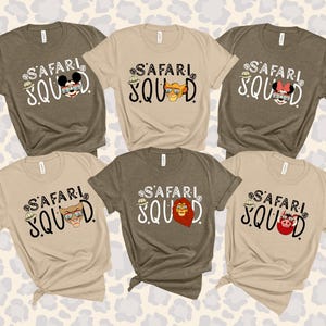 K&ouml;nnte beinhalten: Sechs kurz&auml;rmelige T-Shirts in verschiedenen neutralen Farben, jeweils mit den Worten "SAFARI SQUAD" in einer verspielten Schriftart. Die Shirts haben Cartoon-Charakter-Designs, darunter eine Maus, ein L&ouml;we und ein Schwein mit Safarih&uuml;ten.