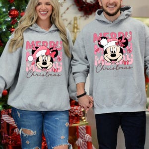 May include: A matching set of gray hoodies with a pink and white "Merry Christmas" design featuring Mickey Mouse. The hoodies have a kangaroo pocket and a drawstring hood.