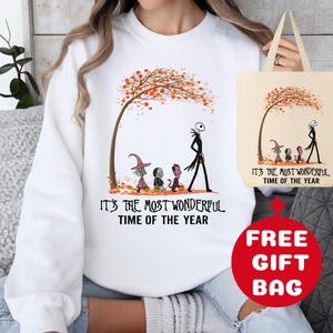 Op de afbeelding: Witte trui met een afbeelding van Jack Skellington en andere personages uit The Nightmare Before Christmas die door een herfstsc&egrave;ne lopen. De tekst "It's the most wonderful time of the year" staat op de trui gedrukt. Een gratis tote bag met dezelfde afbeelding en tekst is inbegrepen.