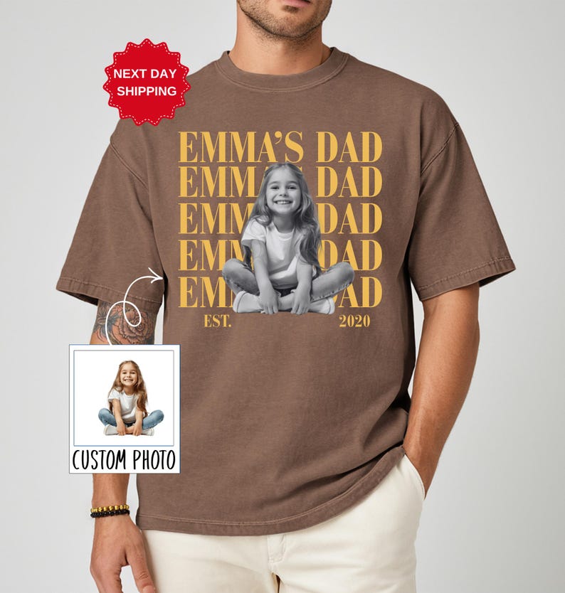 Puede incluir: Camiseta marr&oacute;n con el texto "EMMA'S DAD" repetido verticalmente en dorado, con una foto en blanco y negro de un ni&ntilde;o. La camiseta tambi&eacute;n tiene el texto "EST. 2020" y una etiqueta "CUSTOM PHOTO".
