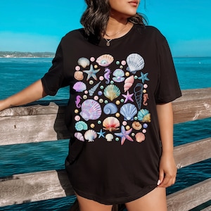 May include: A black t-shirt with a colorful seashell and seahorse pattern. The design features a variety of seashells, seahorses, and pearls in shades of pink, blue, green, and purple.