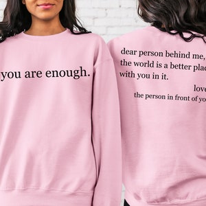 Puede incluir: Sudadera rosa con el texto "you are enough." en la parte delantera y el texto "dear person behind me, the world is a better place with you in it. love, the person in front of you" en la parte trasera.