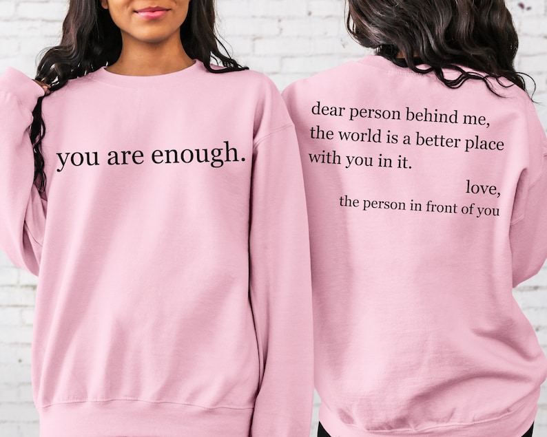 Puede incluir: Sudadera rosa con el texto "you are enough." en la parte delantera y el texto "dear person behind me, the world is a better place with you in it. love, the person in front of you" en la parte trasera.