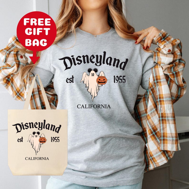 May include: A gray t-shirt with a white tote bag. The t-shirt has a graphic of a ghost holding a pumpkin and the text "Disneyland est 1955 California". The tote bag has the same graphic and text.