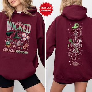 Puede incluir: Sudadera con capucha burdeos con el texto "WICKED CHANGED FOR GOOD" y un gr&aacute;fico de un sombrero de bruja, una escoba y otros elementos m&aacute;gicos. La parte trasera de la sudadera presenta un dise&ntilde;o similar con un sombrero de bruja y una escoba.
