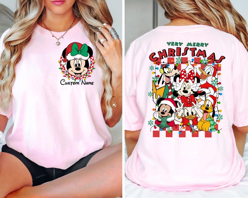 Op de afbeelding: Roze T-shirt met een kerstthema met Mickey Mouse en andere Disney-figuren. De voorkant van het shirt heeft een afbeelding van Mickey Mouse met een kerstmanmuts en de tekst "Custom Name". De achterkant van het shirt heeft de tekst "Very Merry Christmas" en een afbeelding van Mickey Mouse, Minnie Mouse, Donald Duck, Goofy, Pluto en Daisy Duck.