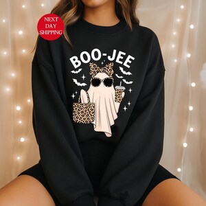 May include: Black sweatshirt with a graphic of a ghost wearing sunglasses and a leopard print bow, holding a leopard print tote bag and a coffee cup. The text "BOO-JEE" is above the ghost. Bats and stars surround the ghost.