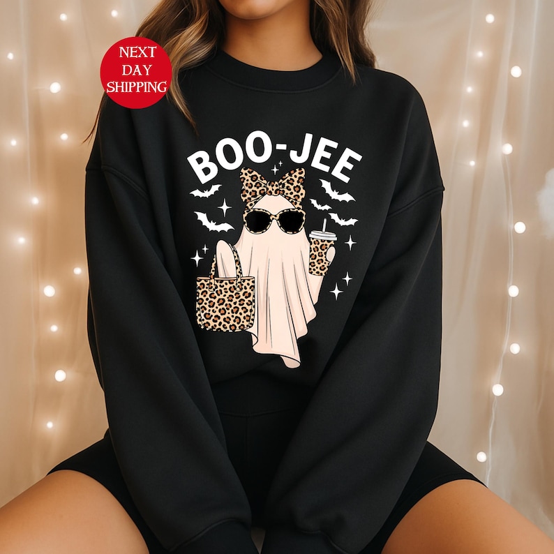 May include: Black sweatshirt with a graphic of a ghost wearing sunglasses and a leopard print bow, holding a leopard print tote bag and a coffee cup. The text "BOO-JEE" is above the ghost. Bats and stars surround the ghost.