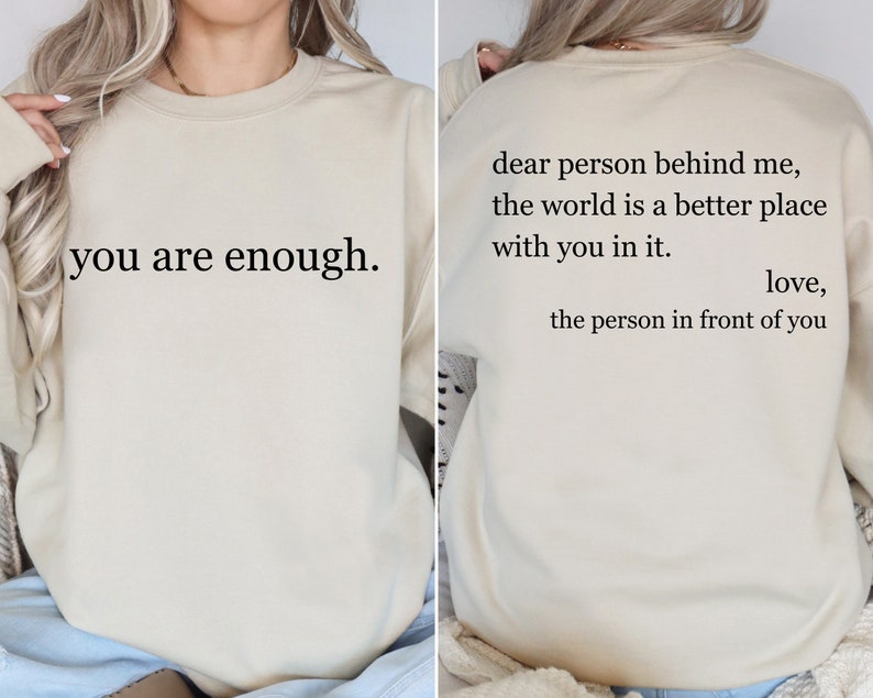 Puede incluir: Una sudadera beige con el texto "you are enough." impreso en la parte delantera y el texto "dear person behind me, the world is a better place with you in it. love, the person in front of you" impreso en la parte trasera.