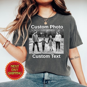 May include: A charcoal gray short-sleeve t-shirt featuring a rectangular black and white photograph of a family of four standing outdoors. The text Custom Photo is printed above the image and Custom Text is printed below the image.