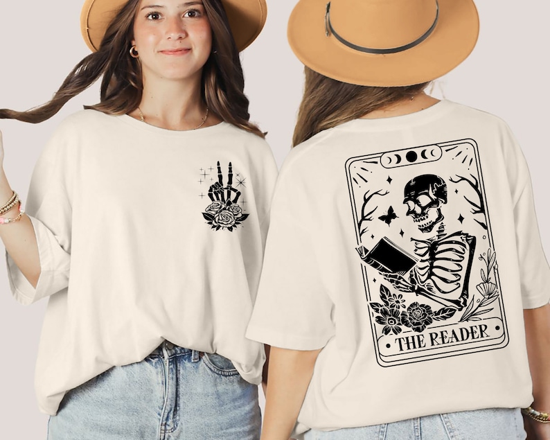 以下が含まれることがあります： 黒い骨格が本を読んでいる白いTシャツ。骨格の周りは花で飾られています。骨格の下には「THE READER」という文字があります。Tシャツの裏面には、黒い平和マークと花が描かれています。