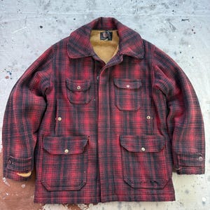Peut inclure: Veste à carreaux rouges et noirs avec quatre poches avant et un col. La veste a une fermeture boutonnée et une doublure beige. Les manches ont des poignets boutonnés. La veste est faite d'une matière épaisse et chaude.
