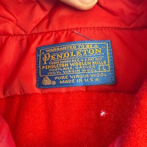 Puede incluir: Un interior de prenda acolchada de color rojo brillante con una etiqueta de tela azul rectangular con texto dorado que dice Warranted to be a Pendleton, Pendleton Woolen Mills, Portland, Oregon, 100% Virgin Wool, talla L y Made in U.S.A.