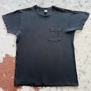 Könnte beinhalten: Ein einfarbig schwarzes Kurzarm-T-Shirt mit Rundhalsausschnitt und einer einzelnen aufgesetzten Tasche auf der linken Brustseite. Das Kleidungsstück hat eine Standardpassform mit geraden Ärmelsäumen und einem geraden Saum am unteren Ende.