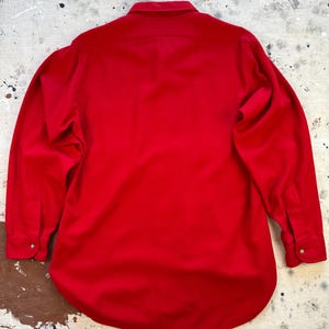 Puede incluir: Una camisa de manga larga con botones en un color rojo vibrante y s&oacute;lido. La camisa presenta un cuello cl&aacute;sico, un canes&uacute; en la espalda y pu&ntilde;os al final de cada manga, cada uno asegurado con un peque&ntilde;o bot&oacute;n. La tela parece tener una textura lisa.