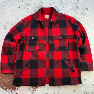 May include: A red and black plaid jacket with two chest pockets and two lower pockets. The jacket has a collared neckline and is made of a thick, warm material. The jacket is open, revealing the interior lining.