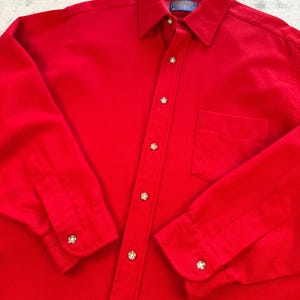 Puede incluir: Una camisa de manga larga de color rojo brillante con botones, cuello cl&aacute;sico, un bolsillo en el pecho y botones de color claro. La etiqueta interior del cuello muestra la marca Pendleton. La camisa tiene un corte estructurado con pu&ntilde;os abotonados.