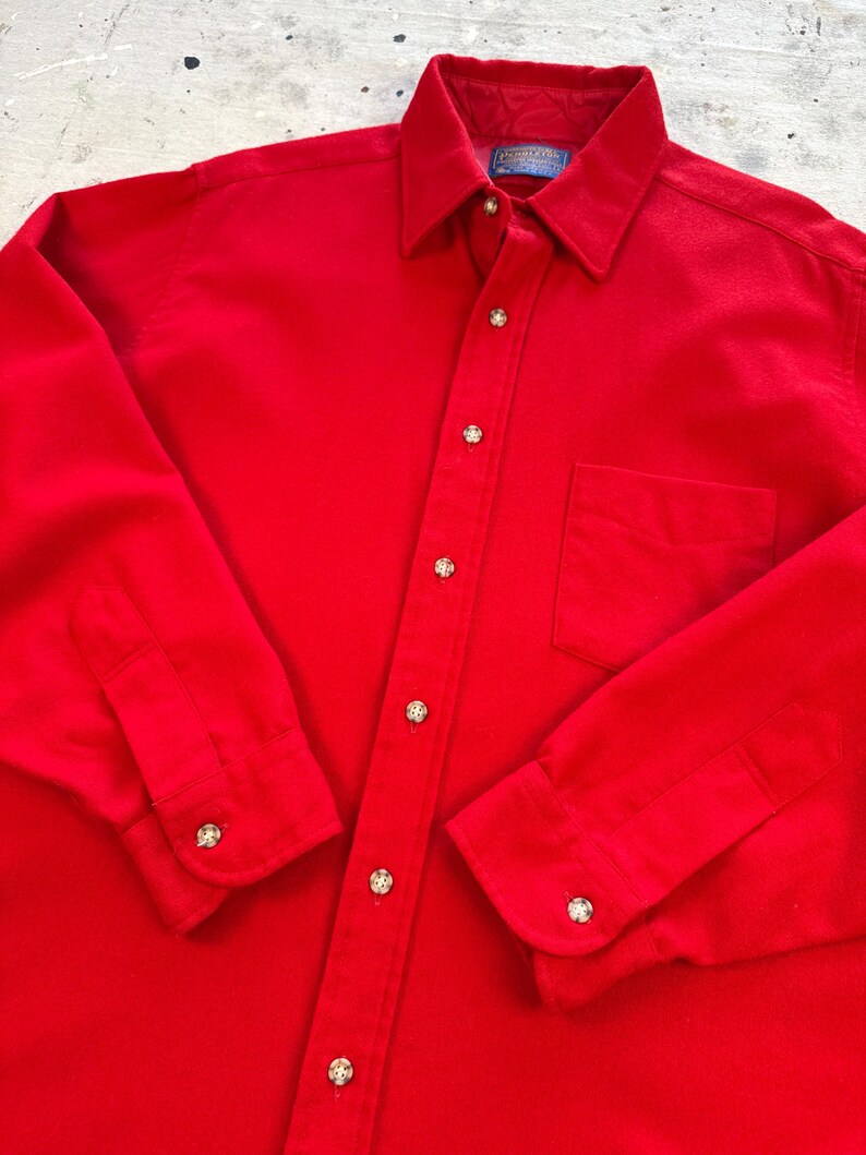 Puede incluir: Una camisa de manga larga de color rojo brillante con botones, cuello cl&aacute;sico, un bolsillo en el pecho y botones de color claro. La etiqueta interior del cuello muestra la marca Pendleton. La camisa tiene un corte estructurado con pu&ntilde;os abotonados.