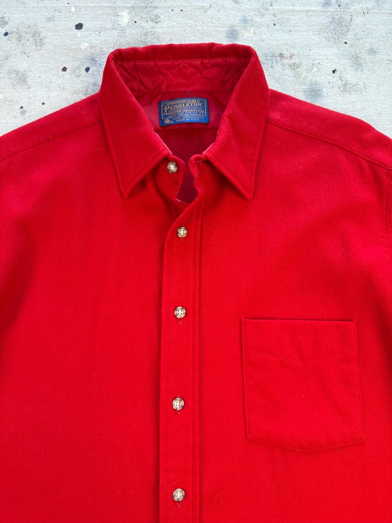 Puede incluir: Una camisa de manga larga de color rojo brillante con cuello cl&aacute;sico, tapeta frontal con botones met&aacute;licos y un bolsillo en el pecho. El interior del cuello incluye una etiqueta azul de la marca Pendleton y un forro rojo acolchado.