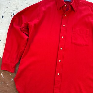 Puede incluir: Una camisa de manga larga en color rojo s&oacute;lido con cuello en punta, un bolsillo en el pecho y una serie de botones redondos de color claro en la parte frontal. La etiqueta interior del cuello muestra la marca Pendleton.