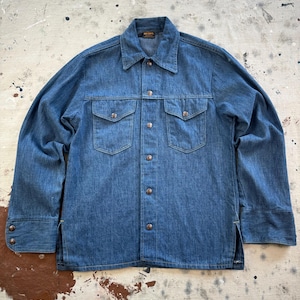 May include: A blue denim long-sleeve shirt featuring a pointed collar, a front button-down closure with metallic buttons, two chest pockets with buttoned flaps, and side slits at the hem. The interior neck label displays the text Big Yank.