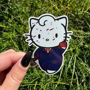 Puede incluir: Un gato de dibujos animados blanco con manchas rojas, vistiendo un traje azul y una corbata roja, sosteniendo un coraz&oacute;n rojo. El gato tiene un fondo blanco.