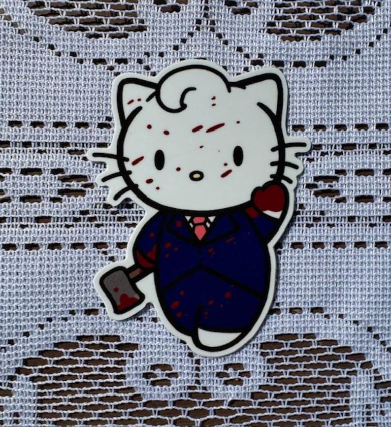 Puede incluir: Un personaje blanco de Hello Kitty con salpicaduras de sangre roja en su cara y traje. Est&aacute; sosteniendo un hacha ensangrentada en su mano derecha. El personaje lleva un traje azul oscuro con una corbata roja.