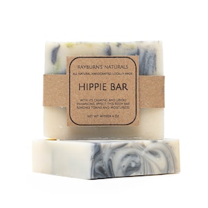 May include: Two bars of handmade soap, one stacked on top of the other. The top bar has a brown paper band with the text "HIPPIE BAR". The soap is white with gray swirls and the label says "NET WT: APPROX 4 OZ".