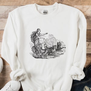May include: White sweatshirt with a black and white illustration of a woman riding in a chariot pulled by a dog.