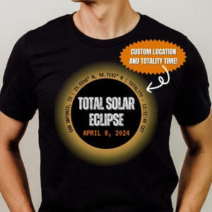 May include: Black t-shirt with a graphic of a total solar eclipse. The graphic includes the date, time, and location of the eclipse. The text reads "TOTAL SOLAR ECLIPSE APRIL 8, 2024 SAN ANTONIO, TX | 29.5598° N, 98.7192° W | TOTALITY - 13:32:45 CDT".