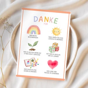 May include: A rectangular card with a peach border features the German word "DANKE" in colorful letters. The card includes illustrations of a rainbow, sun, plant, blocks, an open book, and a heart, with German phrases below each image.