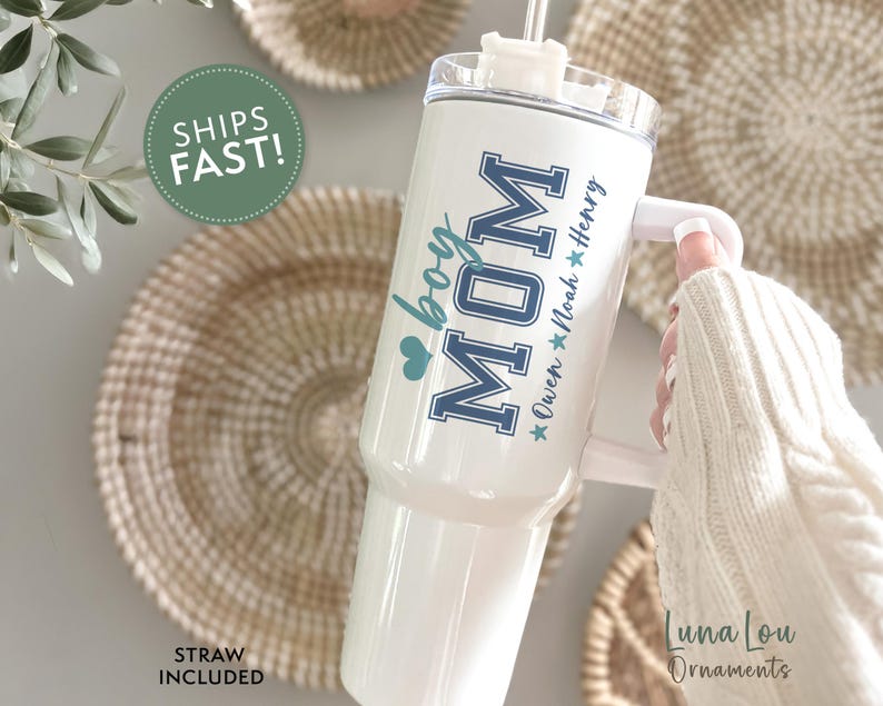 May include: White stainless steel tumbler with a blue and white design that says "Mom" with a heart and "boy" underneath. The tumbler has a handle and a straw. The text below the design says "Owen * Noah * Henry"