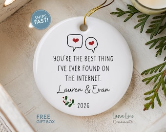 May include: A round white ceramic ornament featuring two speech bubbles with red hearts, the text "YOU'RE THE BEST THING I'VE EVER FOUND ON THE INTERNET.", the names "Lauren & Evan", a small green and red holly sprig graphic, and the year "2026".