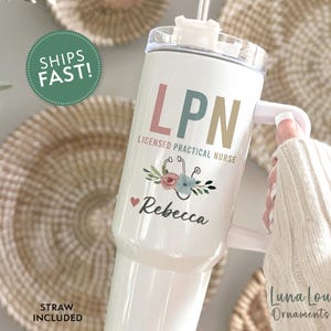 May include: White tumbler with the text "LPN Licensed Practical Nurse" in pink, green, and tan. The tumbler has a floral and stethoscope design, with the name "Rebecca" below. A straw is included.
