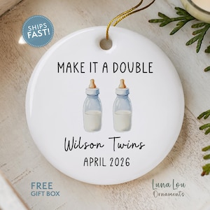 May include: White ceramic ornament with a gold string for hanging. The ornament features the text "MAKE IT A DOUBLE" above two baby bottle illustrations. Below, it reads "Wilson Twins APRIL 2026".
