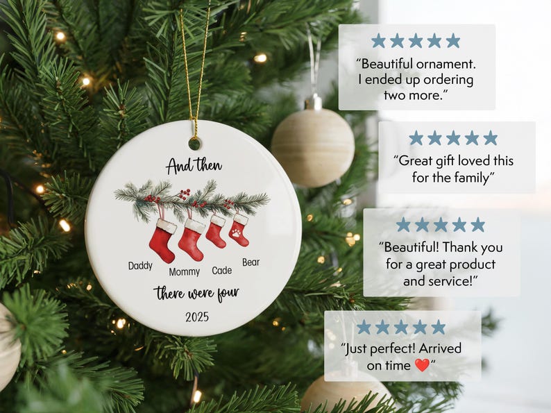 May include: A white ceramic Christmas ornament with a gold string, hanging on a Christmas tree. The ornament features red stockings, text that reads "And then there were four 2025", and names: Daddy, Mommy, Cade, and Bear.
