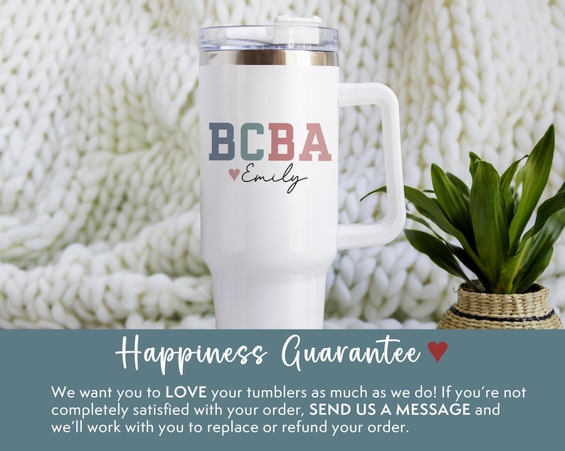 May include: White tumbler with a handle, featuring the text "BCBA" in blue, green, and red, with "Emily" below. A small heart symbol is included. The tumbler has a clear lid and is set against a white knitted background.