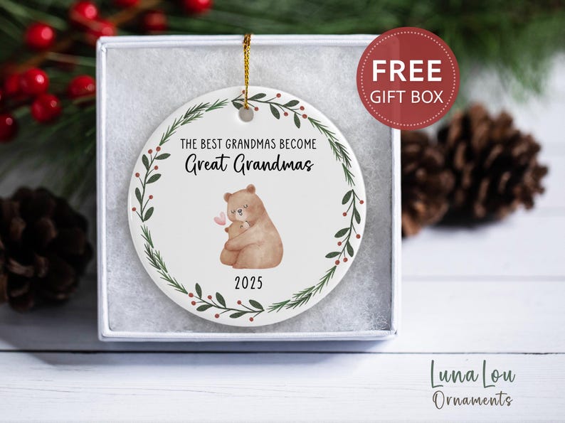 May include: A white ceramic ornament with a gold string, featuring a bear hugging a baby bear, a floral wreath, and the text "The Best Grandmas Become Great Grandmas 2025." The ornament is in a gift box with a "FREE GIFT BOX" sticker.