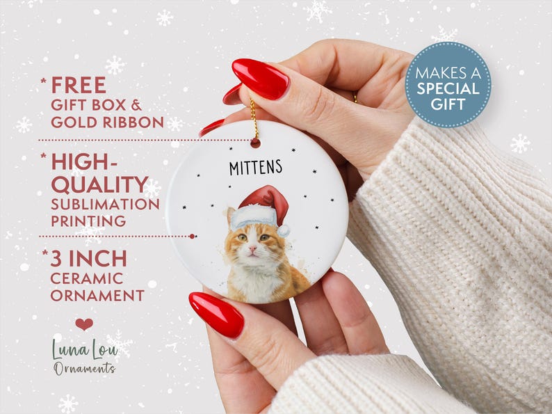 May include: A round white 3 inch ceramic ornament featuring a printed illustration of an orange tabby cat wearing a red and white Santa hat. The name MITTENS is printed in black above the cat, surrounded by small black dots on the surface.