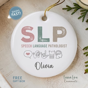 May include: White ceramic ornament with the text "SLP SPEECH LANGUAGE PATHOLOGIST" in pink, green, and brown. Includes icons and the name "Olivia". A gold string is attached for hanging. The ornament is a gift item.