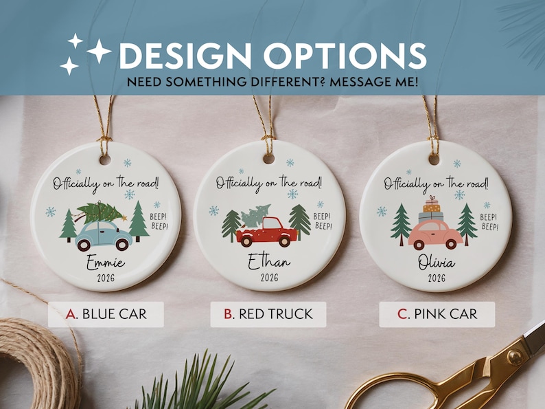 May include: Three round white ceramic ornaments with gold hanging strings. Each features the text 'Officially on the road!' and 'BEEP! BEEP!'. Designs include a blue car, a red truck, and a pink car, each with trees, snowflakes, names, and 2026.