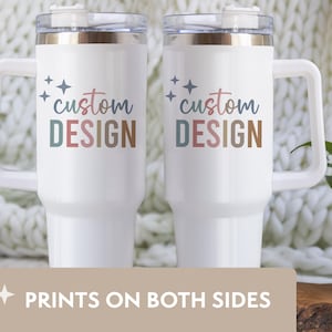 May include: Two white travel mugs with handles, featuring the text "custom DESIGN" in colorful lettering. The mugs have a clear lid and a handle. The bottom of the image reads "PRINTS ON BOTH SIDES".