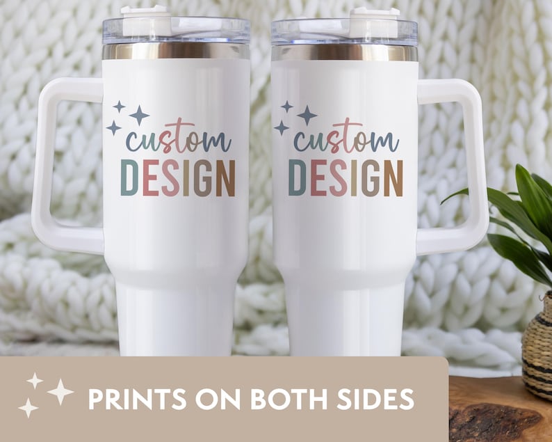 May include: Two white travel mugs with handles, featuring the text "custom DESIGN" in colorful lettering. The mugs have a clear lid and a handle. The bottom of the image reads "PRINTS ON BOTH SIDES".