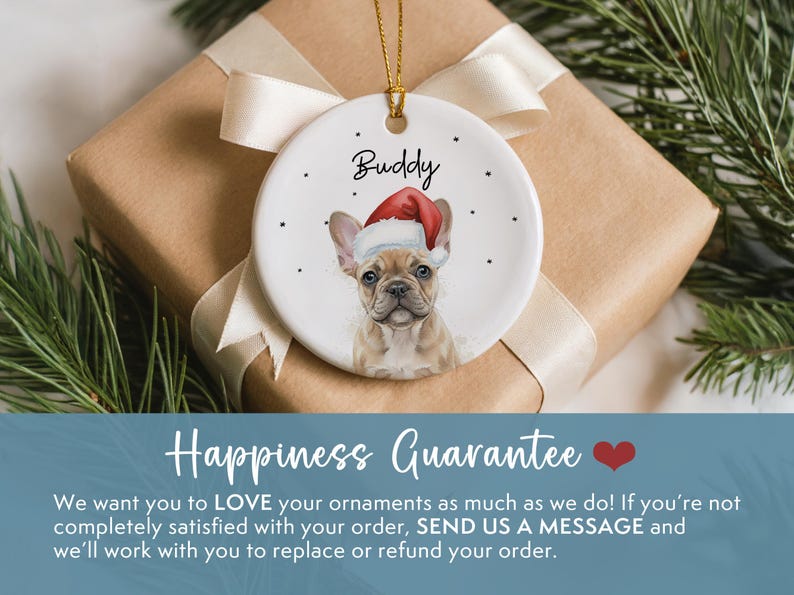 May include: A round white ceramic ornament featuring a tan French Bulldog wearing a red and white Santa hat. The name Buddy is printed in black script above the dog, surrounded by small black dots. A gold string is attached for hanging.
