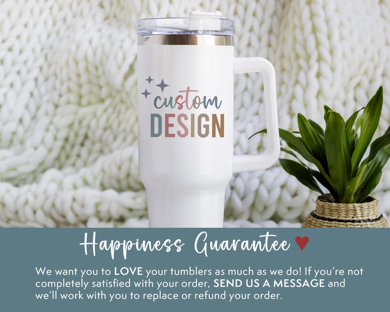 May include: White tumbler with a handle and a clear lid. The tumbler has the words "custom DESIGN" in pastel colors. The tumbler is on a white knitted blanket. A plant in a woven basket is to the right.