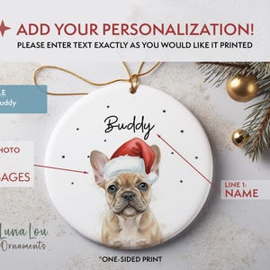 May include: A round white ceramic ornament featuring a tan French Bulldog wearing a red and white Santa hat. The name Buddy is printed in black script above the dog. The ornament includes a gold hanging string and a one-sided print design.