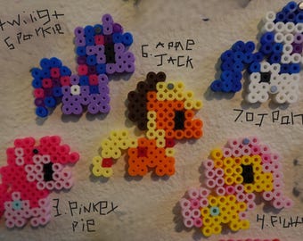 May include: A collection of colorful pony figures made from small, round beads. The ponies are in various colors, including pink, blue, purple, yellow, and orange. Each pony has a unique design and is labeled with a name. The figures are arranged on a white surface.
